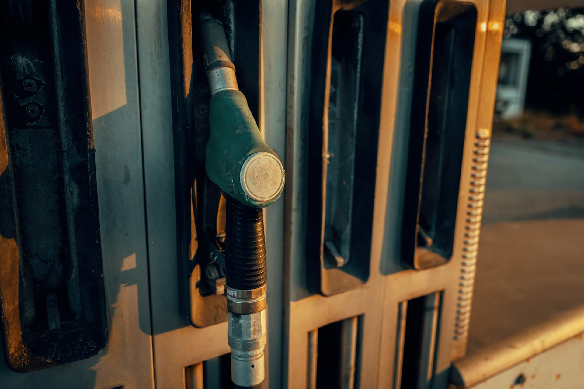 Close-up of a fuel nozzle resting in a gas station pump in warm evening light